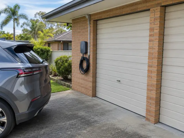 Wall-mounted EV charger on a brick garage wall beside a driveway in a suburban home in Berkeley Vale