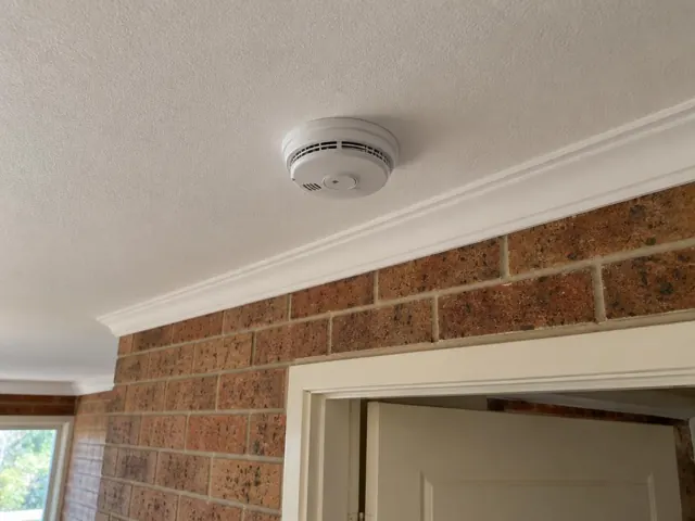 Ceiling-mounted smoke alarm above a brick interior wall and doorway in Glenning Valley