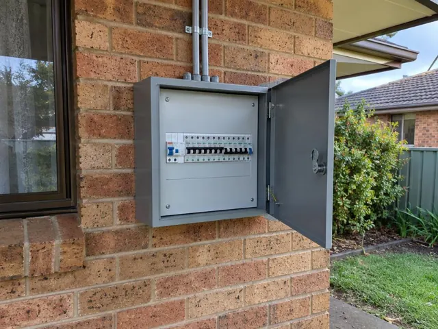 Open outdoor electrical switchboard on a brick house wall beside a window in Berkeley Vale